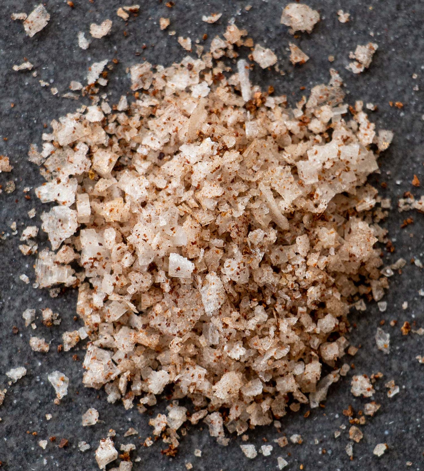 Closeup photo of a pile of green alder flavoured sea salt flakes, on a dark grey slate tile.