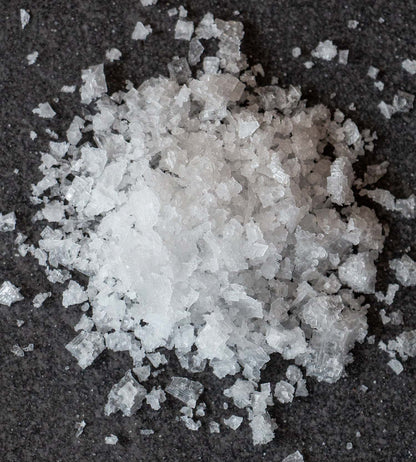 A closeup of white sea salt flakes on a dark grey stone background.